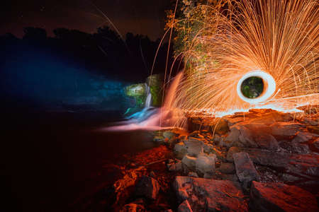 Eerily glowing waterfall at night with yellow orb of sparksの写真素材