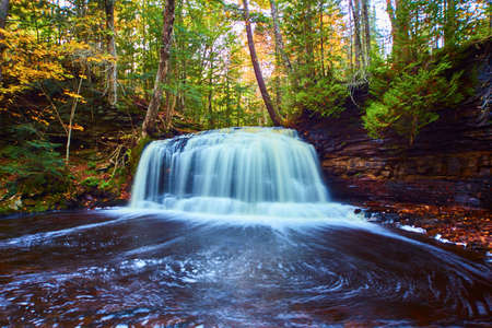Gorgeous waterfall at Rock River Falls and its enormous basin under gorgeous red and brown cliff wallの写真素材