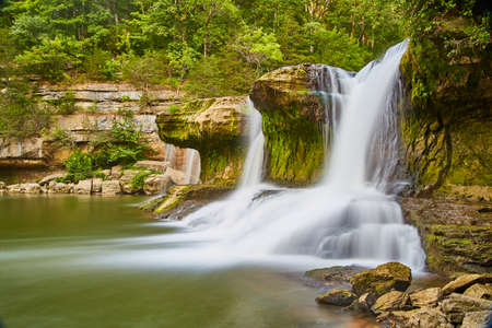 Falls in a jungle type setting with moss on rocks and deep green forestの写真素材