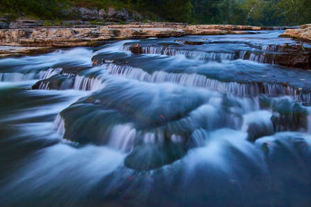 Flowing river and smaller Cataract Falls with a green forest in the background and gentle waterfalls