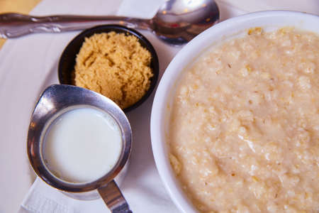 Looking down on traditional and clean bowl of warm breakfast oatmeal with side of brown sugar and milkの写真素材