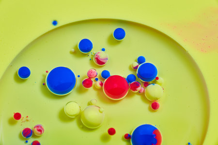 Yellow surface of liquid with small and colorful red and blue ballsの写真素材