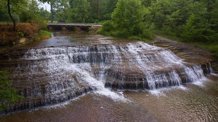 Large cascading waterfalls into river with bridge in backgroundの写真素材