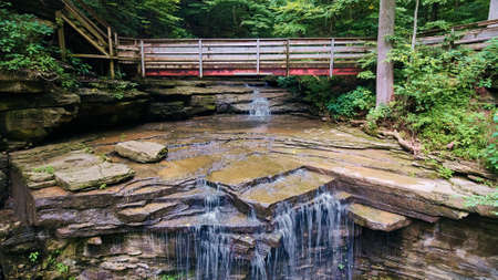 Walking bridge over waterfall as it goes off of large cliffの写真素材