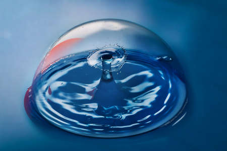 Blue surface with clean bubble containing ripples from two water drops colliding in airの写真素材