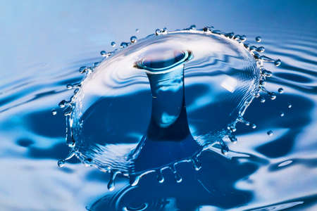 Large splash and ripples as two water drops hit in the air on blue waterの写真素材