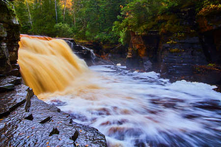 Wet rock path with giant golden and brown waterfall in a deep green forestの写真素材