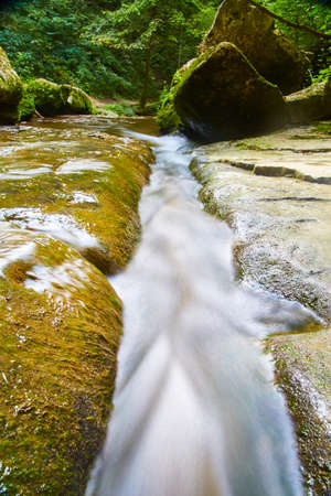 White water current of a stream that flows over rocks and passes between large boulders in a forestの写真素材