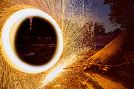 Portal of yellow sparks against craggy stone and rock in front of waterfalls and a fallen tree at...