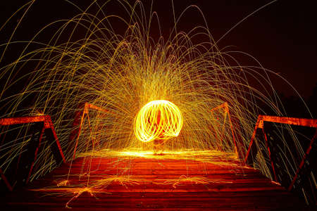 Multiple balls of yellow light from spinning sparks at night on a bridge with a personの写真素材