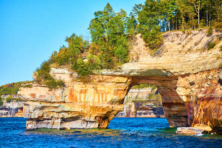 Pictured Rocks with tunnel through the rocks and trees growing atop the archの写真素材