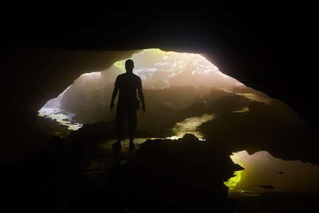 Silhouette of person in cave opening over waterの写真素材