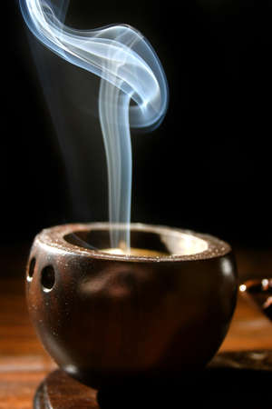 A thin trail of smoke rises from a brown cup-like incense holderの写真素材