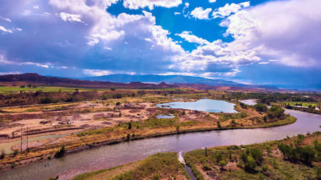 River and pond through desert fields with mountains and rays of sunの写真素材