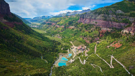 Town tucked into valley of large mountain chain with lush fall aspen tree forestの写真素材