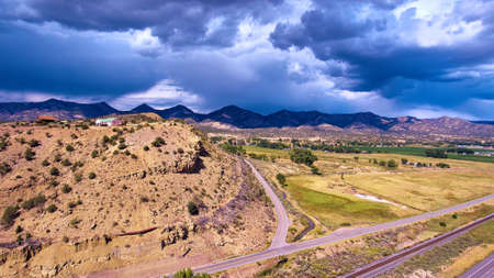 Large mountains with house on hill in desert next to roadsの写真素材