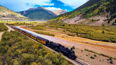 Tourist train with coal leaving small town along river in the mountainsの写真素材
