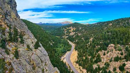 Cliff mountain of rocks next to highway road travelling through pine treesの写真素材