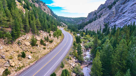 Highway road next to river in canyon surrounded by mountains and pine treesの写真素材