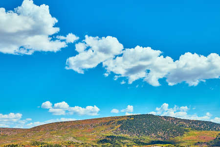 Blue sky with small clouds against colorful hill