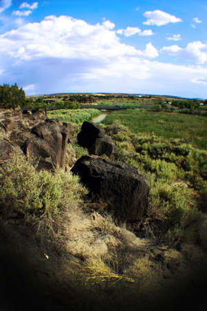 Large boulders sit on a green grassy plain against a blue sky with pillowy white cloudsの写真素材