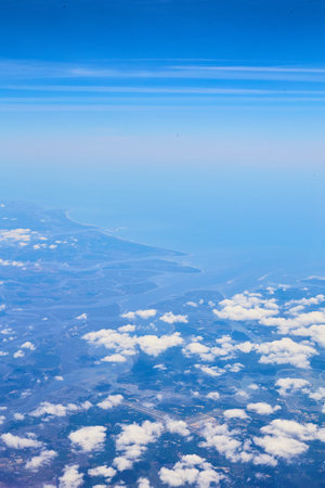 Airplane view of clouds and blue sky with land in distanceの写真素材