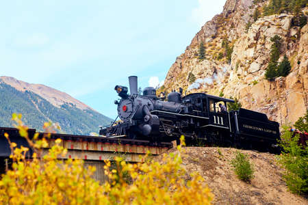 Close up of locomotive train approaching bridge with fall colors and mountains