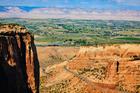 Large red cliff with canyon and road in background and large lush valley with mountainsの写真素材