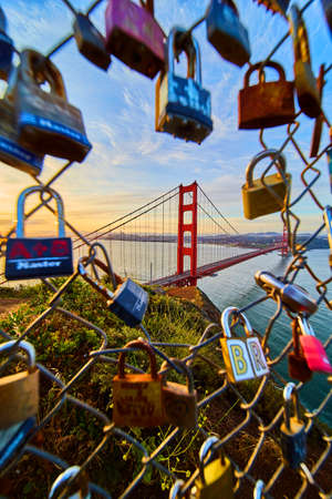 Golden Gate Bridge in California through hole in chain link fence covered in locksの写真素材