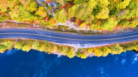 Aerial looking down on road between blue water lake and rocky forest in fallの写真素材