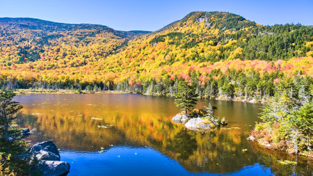 Lake in New Hampshire reflecting colorful peak fall mountains and lone rocky island with pine treeの写真素材