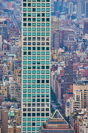 Tall narrow skyscraper of turquoise squares with background of small buildings from above verticalの写真素材