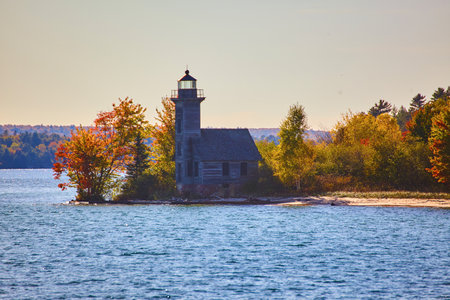 Peninsula with a lighthouse and fall or summer forest and a sandy beach and blue waterの写真素材