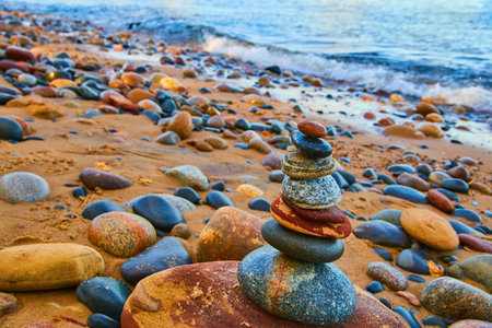 Cairn of stacked smooth lakebed stones with sandy shore and crashing blue wavesの写真素材