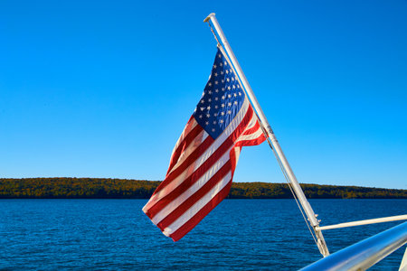 American flag hanging off boat with distant shore and calm lake or river watersの写真素材