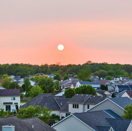 Sun rising setting over suburban homes neighborhood houses green forest tree skyline aerial panoramaの写真素材
