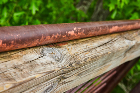 Fading and chipped red paint on metal pole resting on carved wood beam with cracks and wood knotsの写真素材