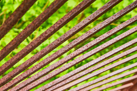 Bright sunlight reflecting silvery off red rusting metal bars with blurry green background assetの写真素材