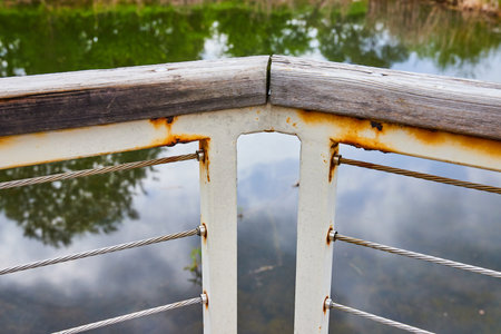 Close up corner piece of wood railing on top of rusty white poles and wires with pond viewの写真素材
