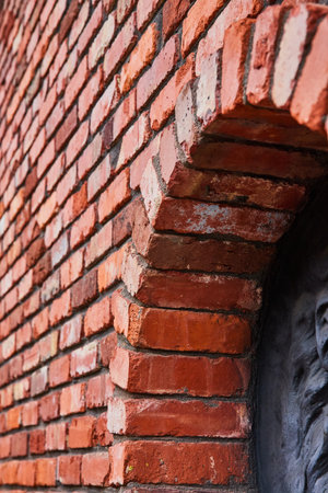 Slanted view of red brick wall and protruding archway with partial black raised motif on right