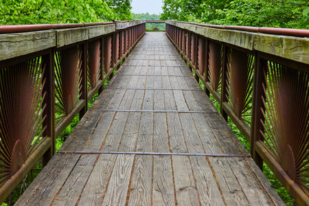 Long view of bridge with worn planks and rusty rising sun pattern on railing barsの写真素材