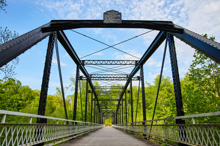 Bright blue sky with white clouds over black metal bridge, lush, green forest backgroundの写真素材