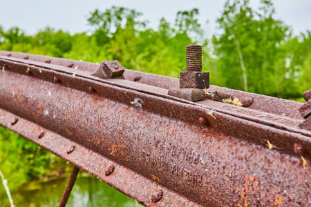 Rusty nuts and bolts on bridge handrail with blurred trees and river in summerの写真素材