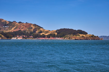 Distant shoreline with red roofed buildings and mountainous hillside and choppy bay waterの写真素材
