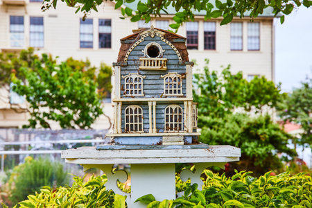 Front of fairy house mansion or bird house on white pedestal with building in backgroundの写真素材