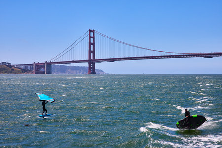 Two men sailboarding on choppy bay waters with Golden Gate Bridge behind themの写真素材