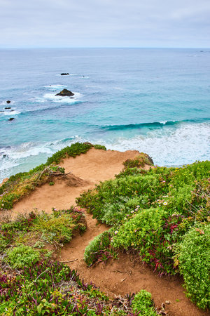 Sandy green trail overlooking scenic teal and navy blue ocean waves breaking against unseen shoreの写真素材