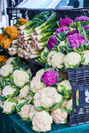 Black crates on table containing variety of colorful cauliflowers and one crate of leaksの写真素材