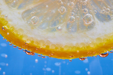 Macro shot of curved edge of see through lemon slice on blue background with fizzy bubblesの写真素材