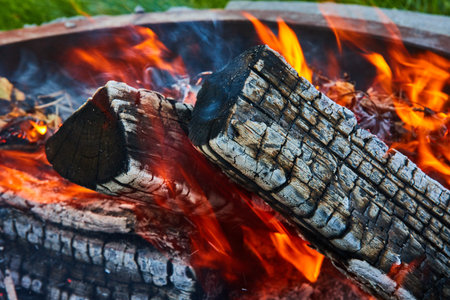 Orange and yellow flames around three logs in firepit close up background asset